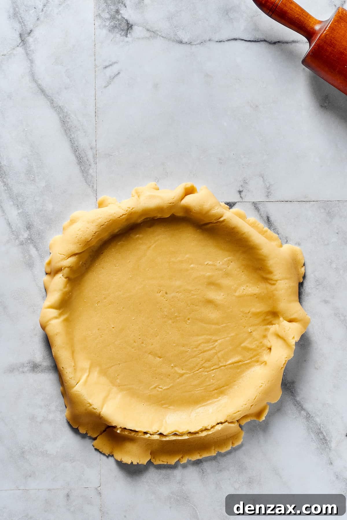 A carefully rolled-out pie crust draped over a pie plate, with the edges generously overhanging the dish, ready for shaping.
