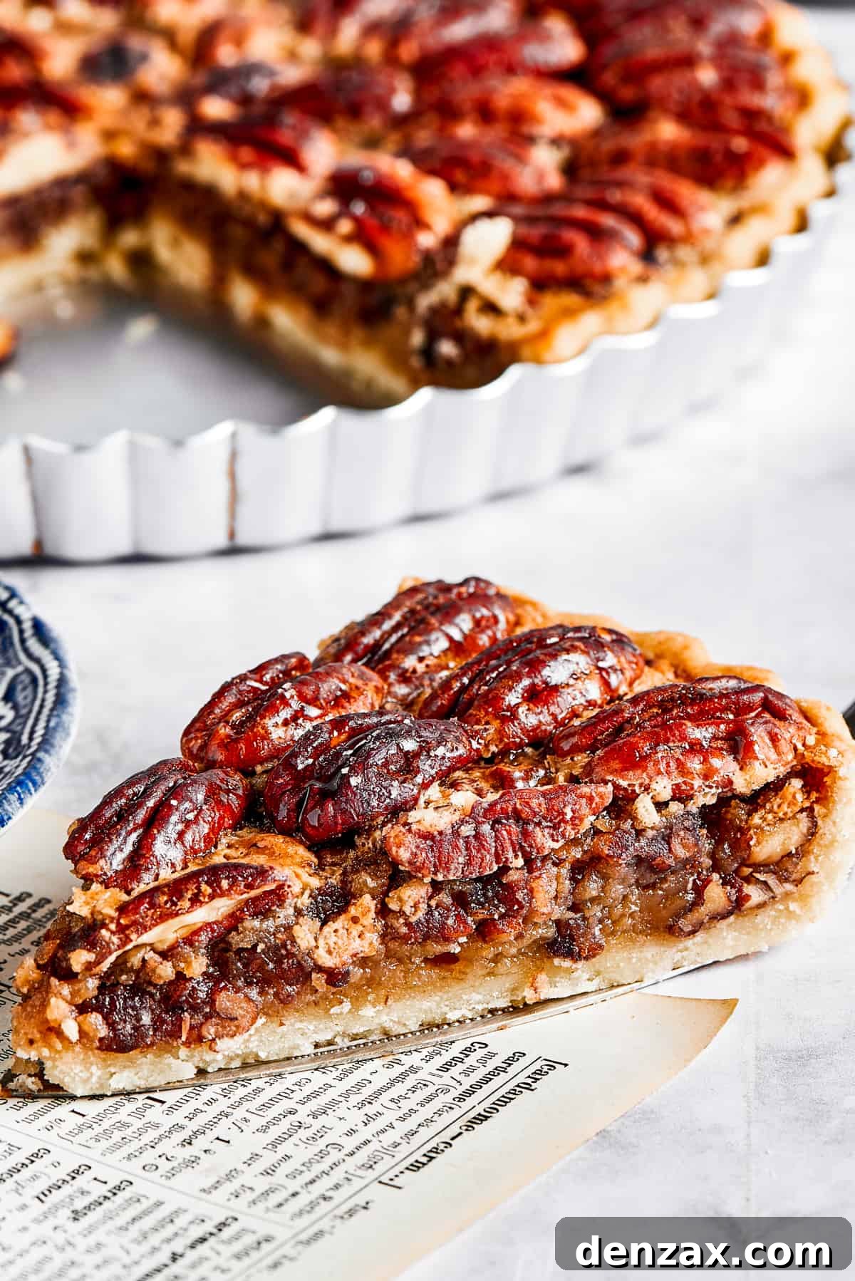 The Best Pecan Pie Recipe is here, easy to make and perfect for your holiday table! You'll love the homemade crust and sweet, nutty filling. A mouth-watering slice of pecan pie resting on a pie server, poised beside the full pie in its dish, ready for serving.