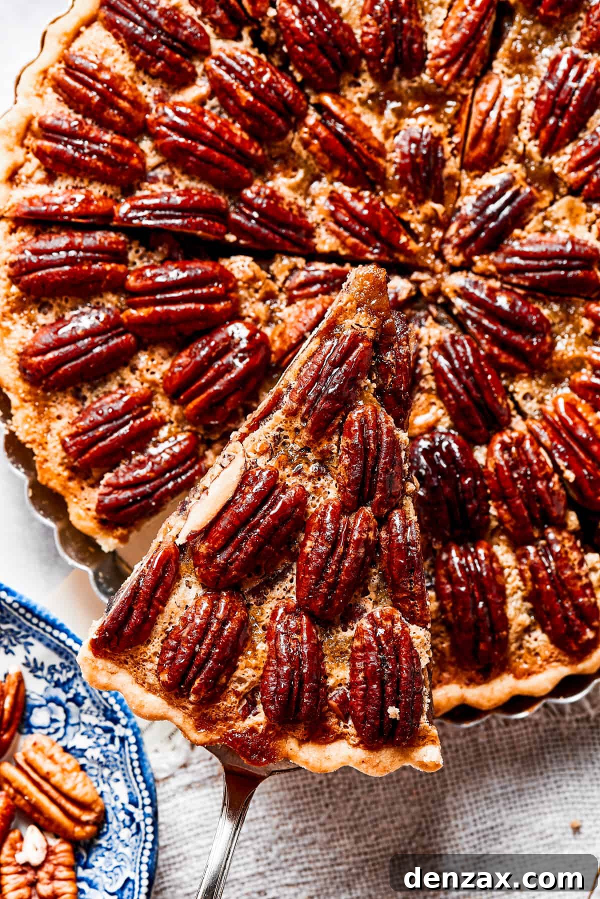 The Best Pecan Pie Recipe is here, easy to make and perfect for your holiday table! You'll love the homemade crust and sweet, nutty filling. A close-up shot of a perfect slice of pecan pie being gently lifted from the pie dish, revealing its thick, golden filling and robust crust.