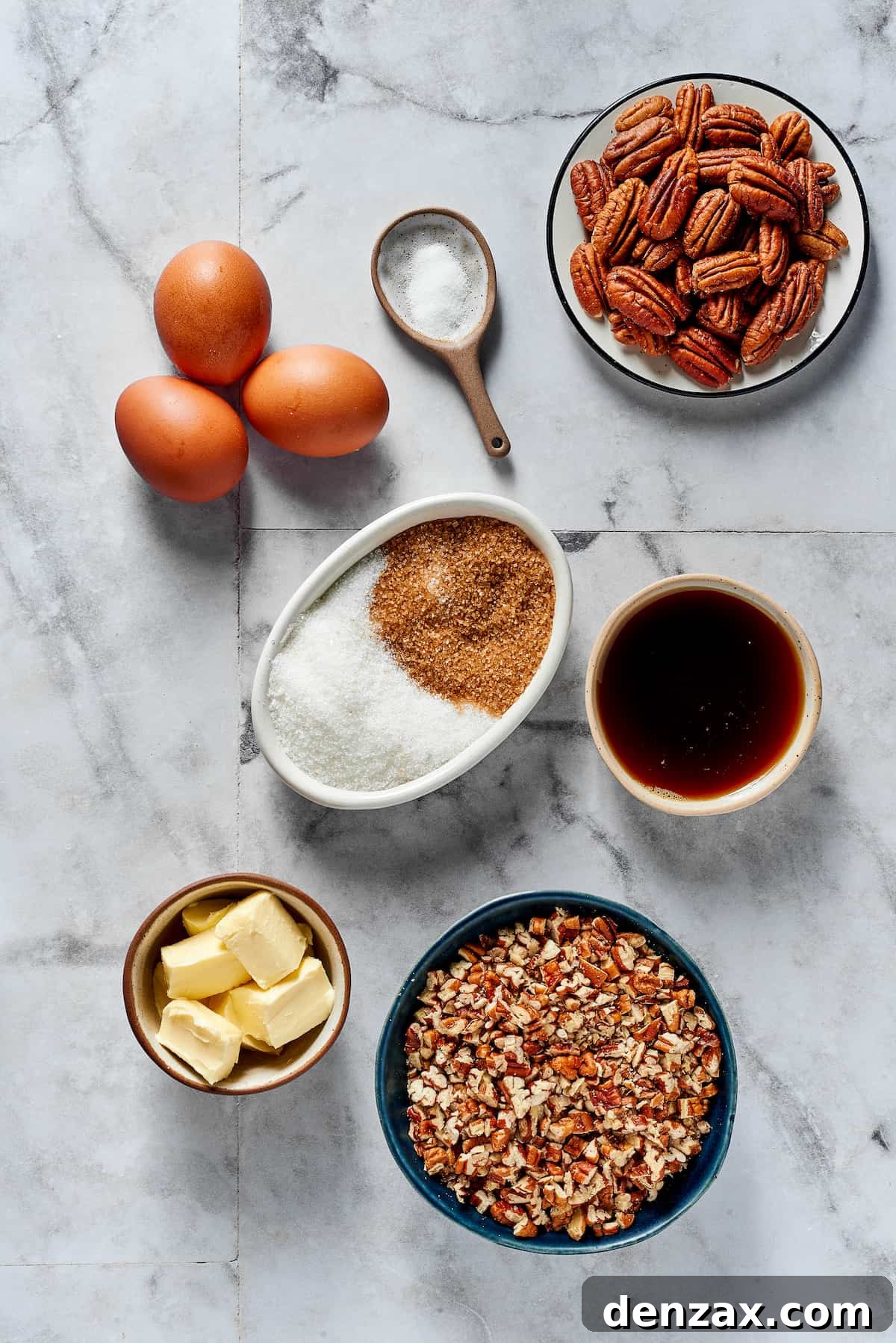 The Best Pecan Pie Recipe is here, easy to make and perfect for your holiday table! You'll love the homemade crust and sweet, nutty filling. An overhead shot showcasing the key ingredients for pecan pie: fresh eggs, a pinch of salt, whole pecans, white and brown sugar, a bottle of maple syrup, soft butter, and a bowl of chopped pecans.