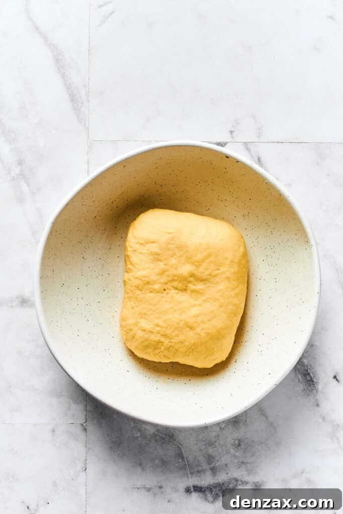 A small rectangle of smooth dough resting in a clean bowl, covered with plastic wrap.