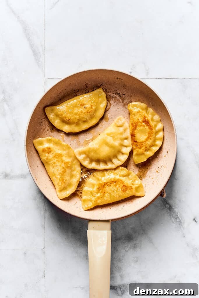 A skillet full of pierogi frying in melted butter, turning golden brown.