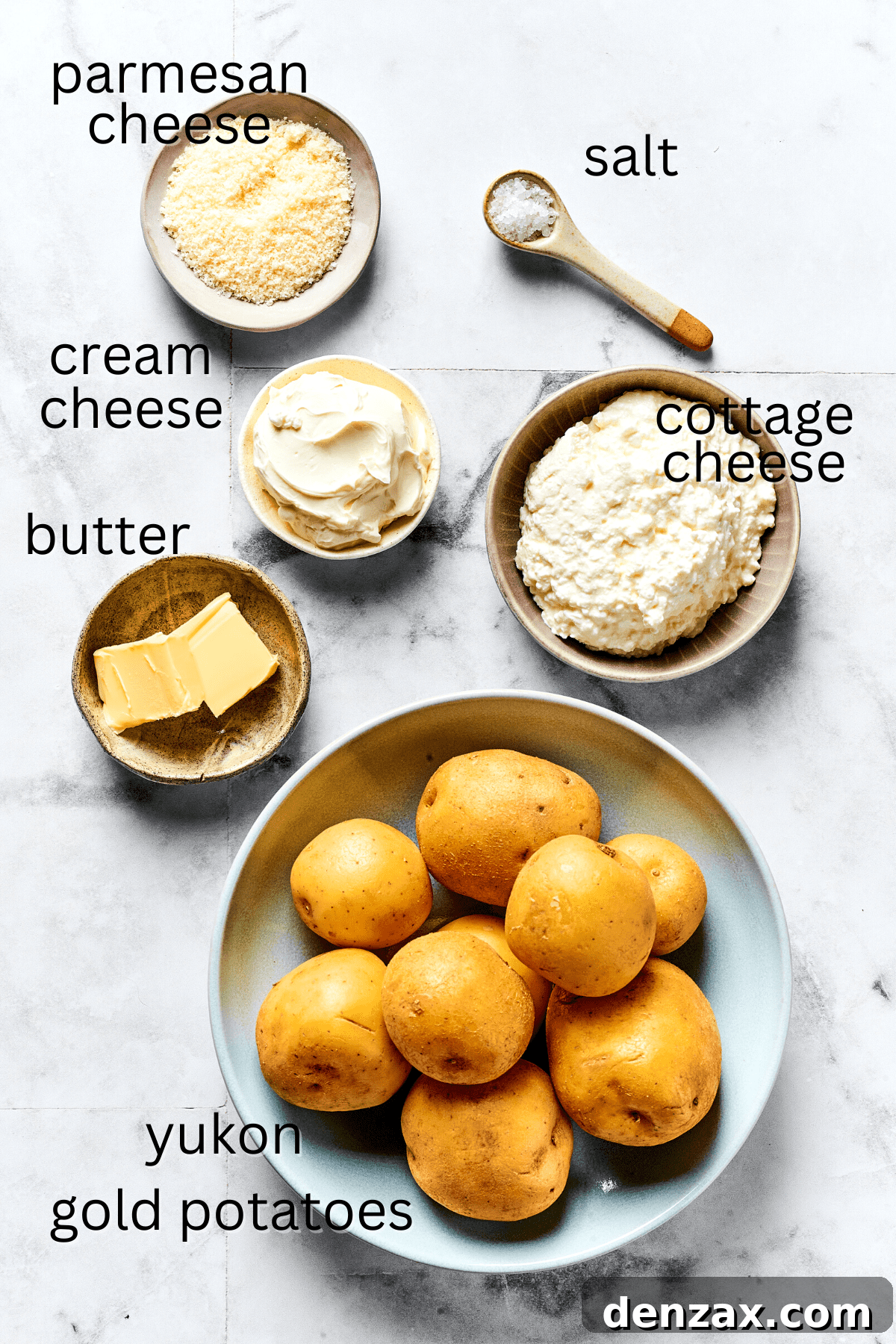 From top: Bowl of grated Parmesan cheese, sea salt, tub of sour cream, cottage cheese, butter sticks, and whole Yukon Gold potatoes.