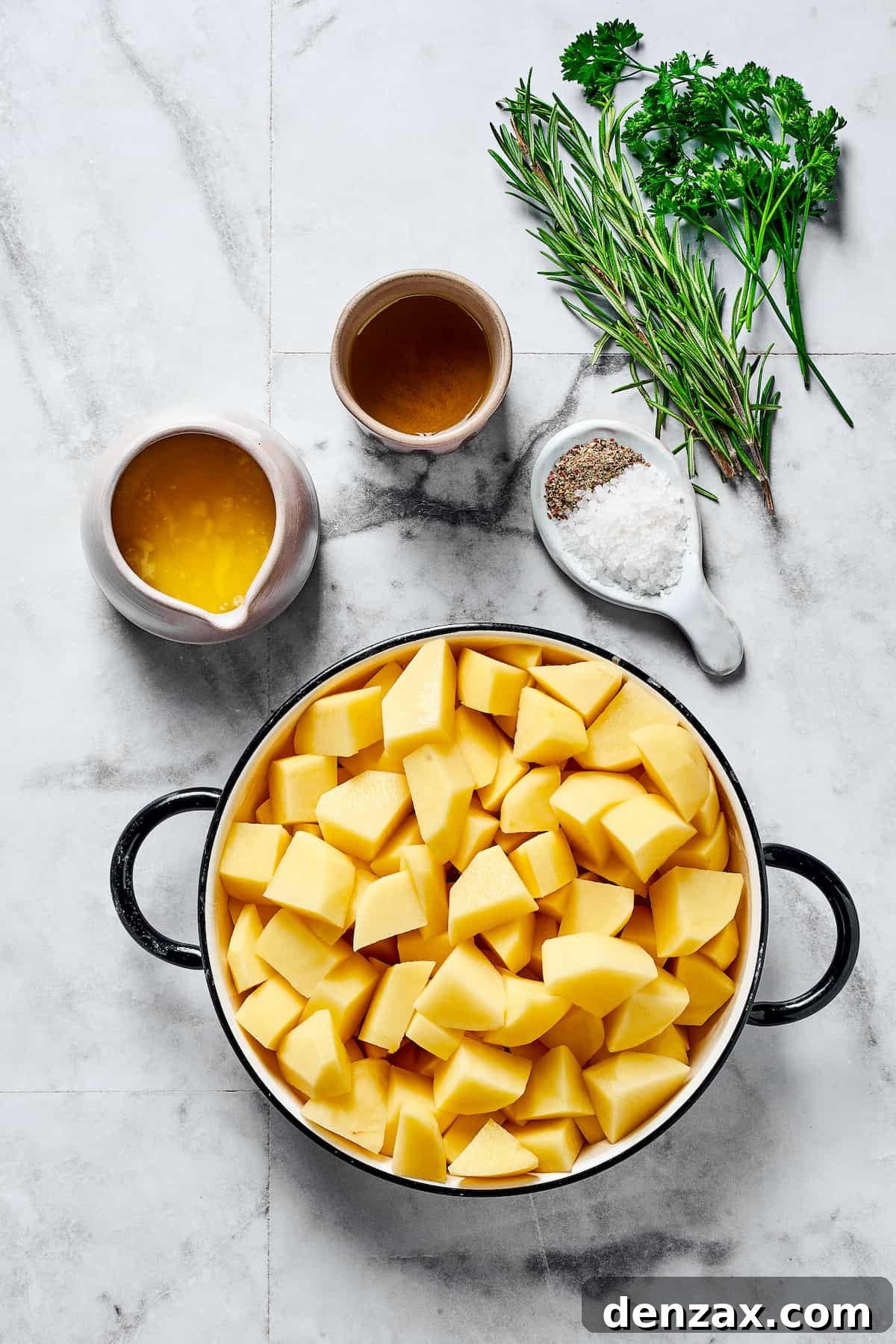From top: Olive oil, fresh rosemary, fresh parsley, melted butter, salt and pepper, and cut raw potatoes, ready for seasoning.