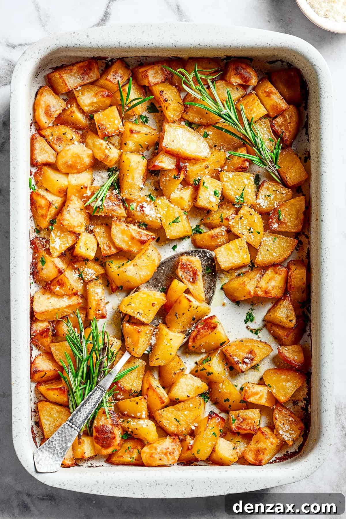 A large baking dish filled with beautifully baked, seasoned potato pieces, golden and crispy.