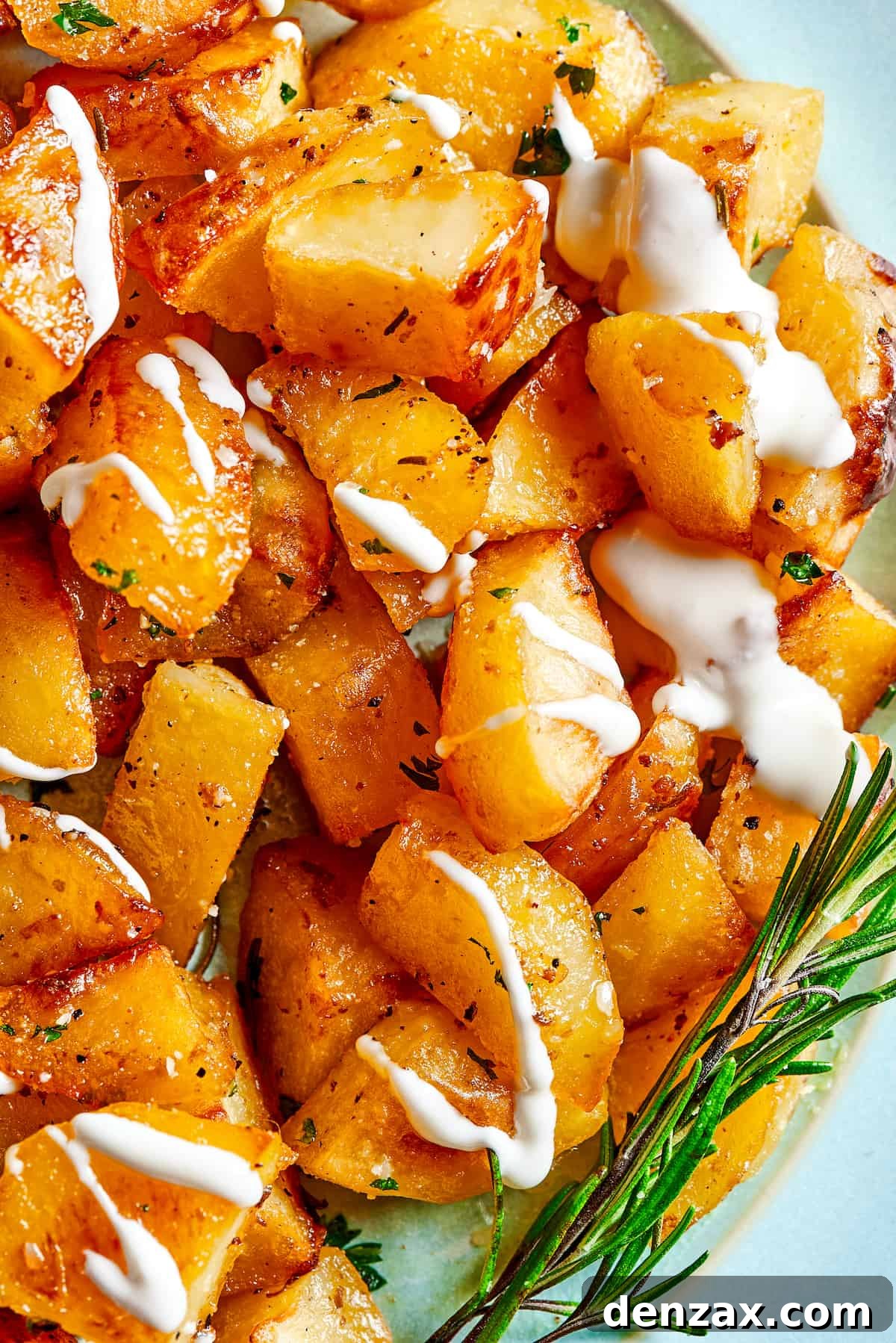 Close-up shot of seasoned roasted potatoes garnished with rosemary and a dollop of yogurt sauce.
