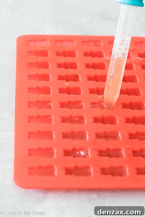 homemade gummy bear mixture being filled into silicone molds with a dropper