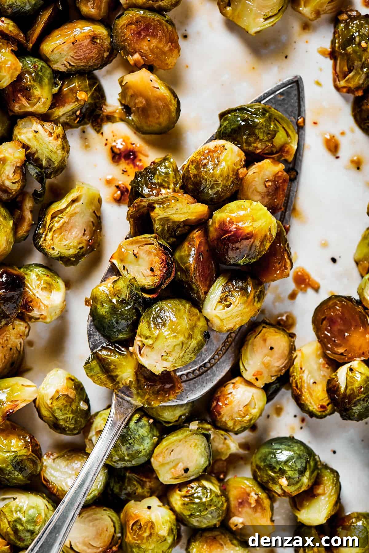A tray of golden-brown roasted Brussels sprouts with a silver serving spoon, ready to be glazed.