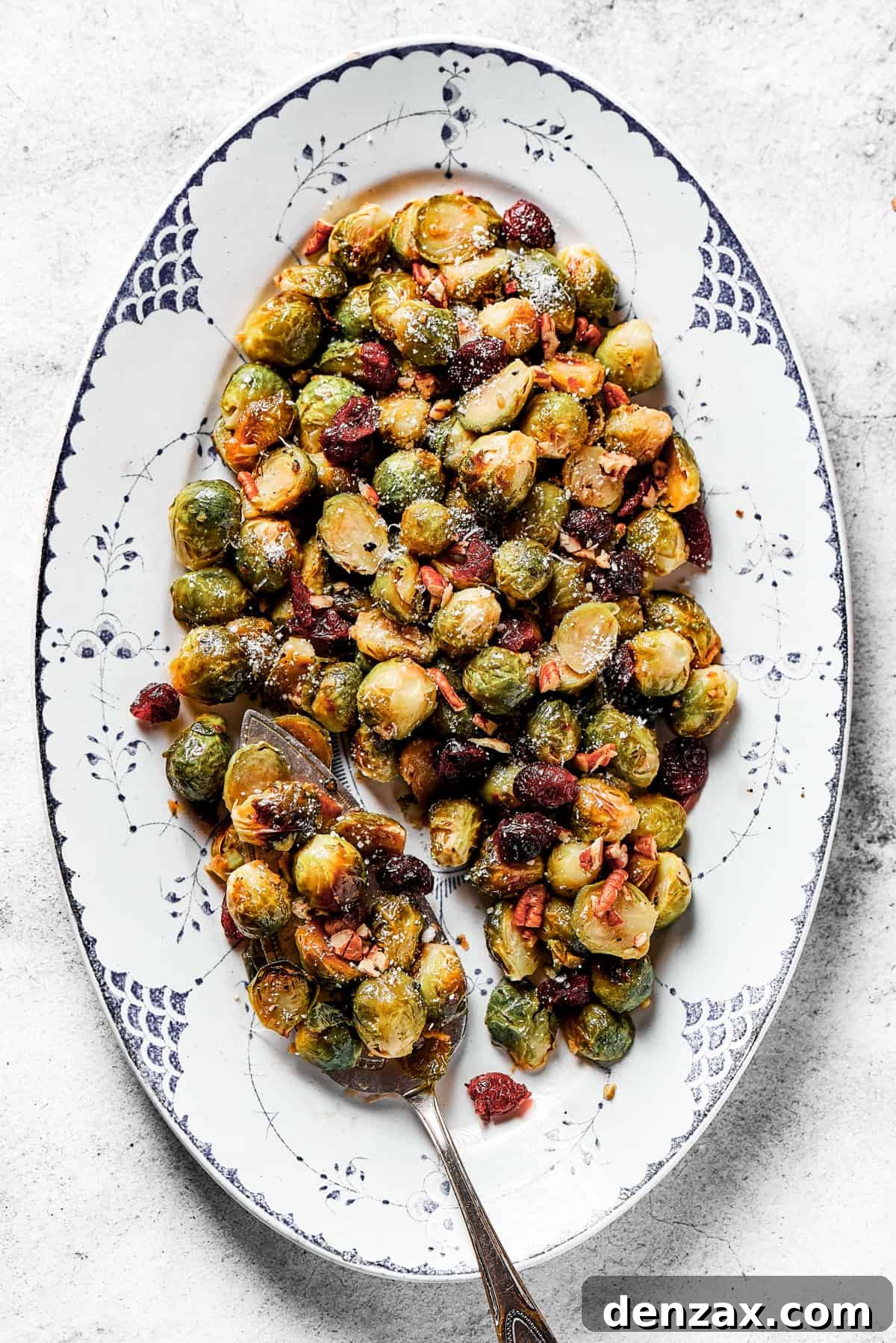 An oval platter brimming with perfectly roasted, glazed Brussels sprouts, garnished with cranberries and pecans.