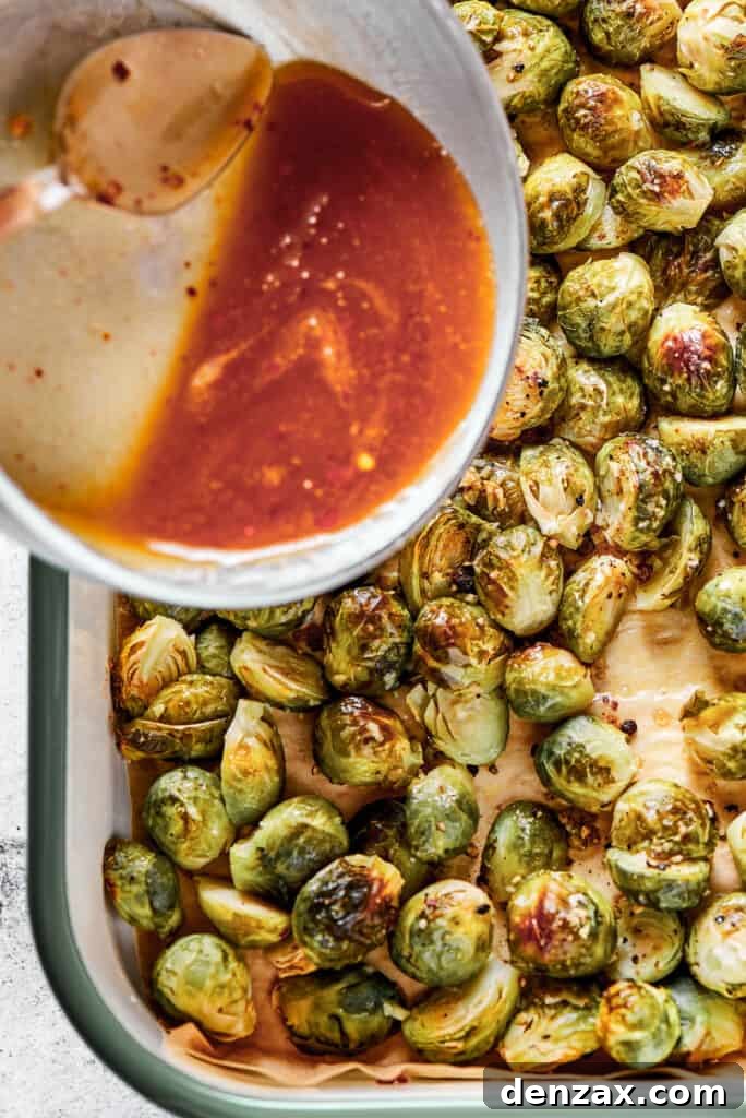 Pouring the glossy maple-pomegranate glaze over a tray of freshly roasted Brussels sprouts.