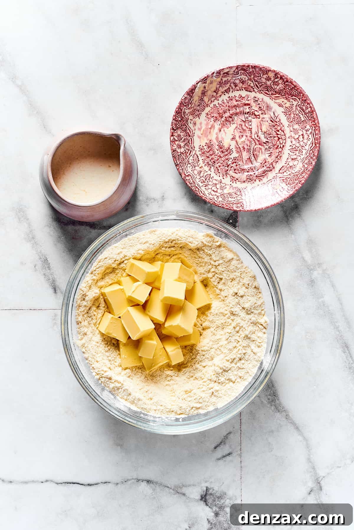 Cold butter cubes being meticulously added to a bowl of dry biscuit ingredients, ready for mixing.