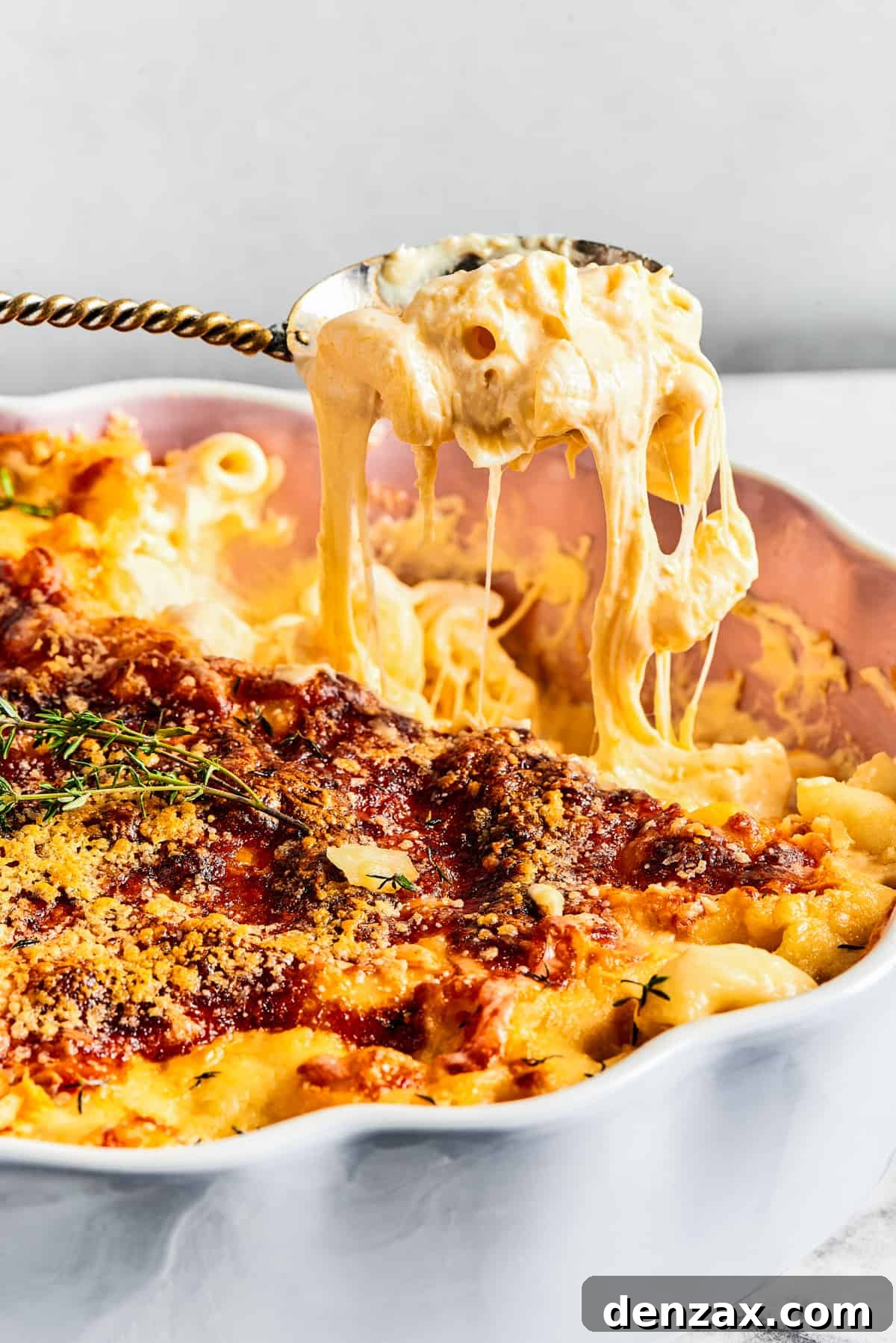 A major family favorite, this ultra-cheesy Baked Macaroni and Cheese is easy to make and perfect for holidays, meatless meals, or anytime! A spoonful of baked mac and cheese being lifted from a decorative fluted baking dish, demonstrating its gooey, stretchy texture.