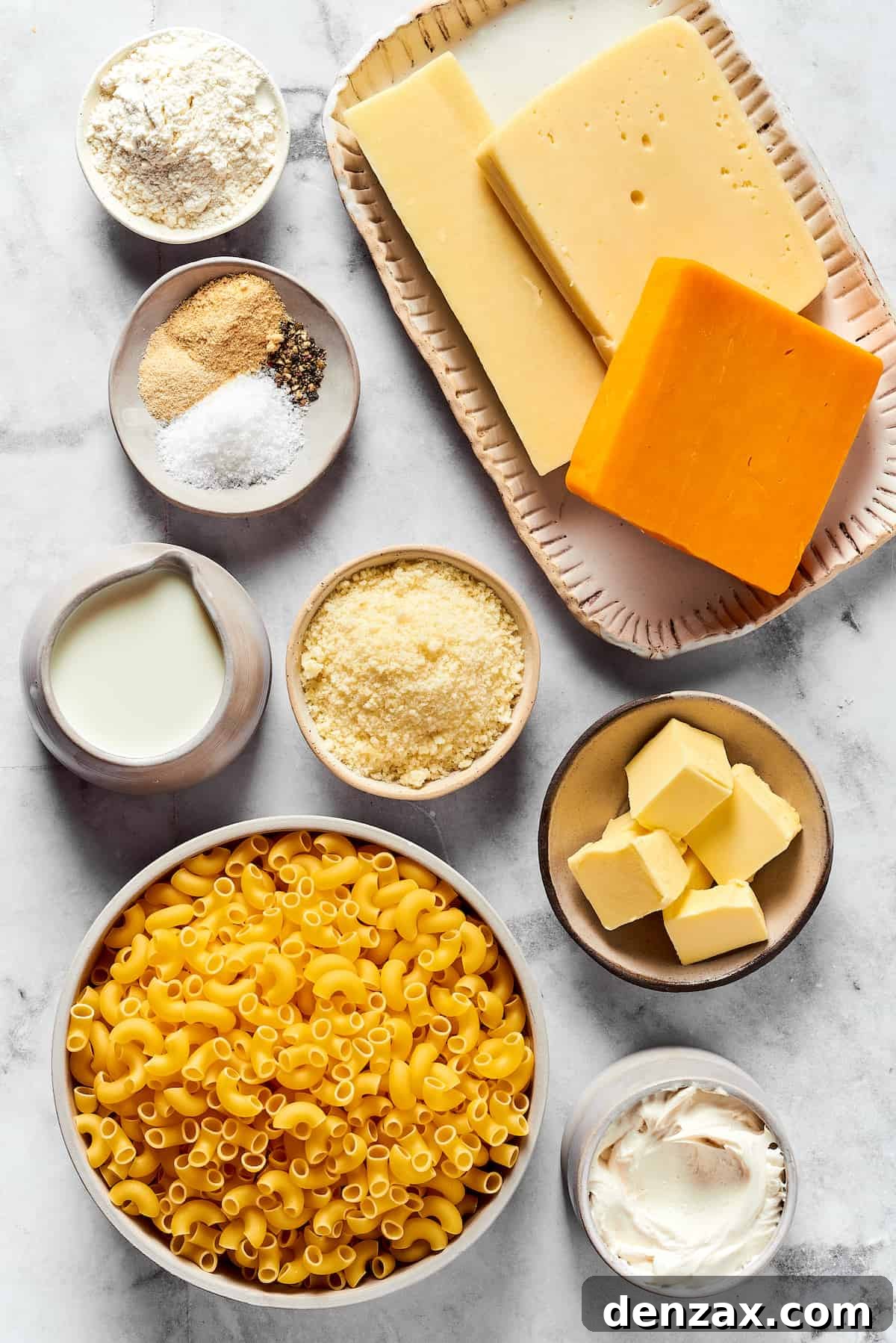 A major family favorite, this ultra-cheesy Baked Macaroni and Cheese is easy to make and perfect for holidays, meatless meals, or anytime! Arrangement of key ingredients for baked mac and cheese: flour, grated Gouda, shredded mozzarella, grated cheddar, various seasonings, milk, Parmesan cheese, butter, elbow macaroni, and heavy cream, laid out on a clean surface.