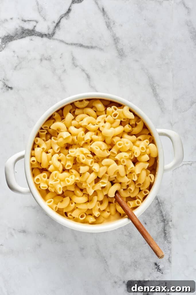 Oven-Baked Cheesy Perfection 6 A large spoon mixing cooked elbow pasta into a rich, creamy cheese sauce in a Dutch oven, ensuring every noodle is coated.