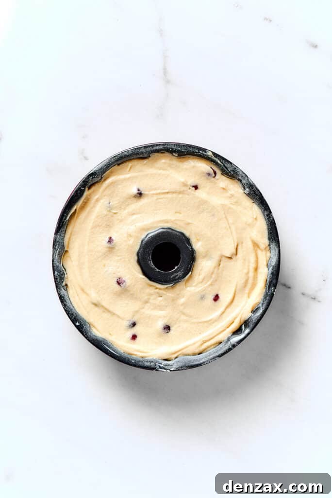 A Bundt pan completely filled with smooth cranberry pound cake batter, ready for baking.