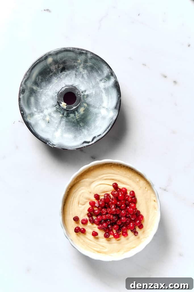 A buttered and floured Bundt pan ready for batter, next to a mixing bowl of cranberry pound cake batter.