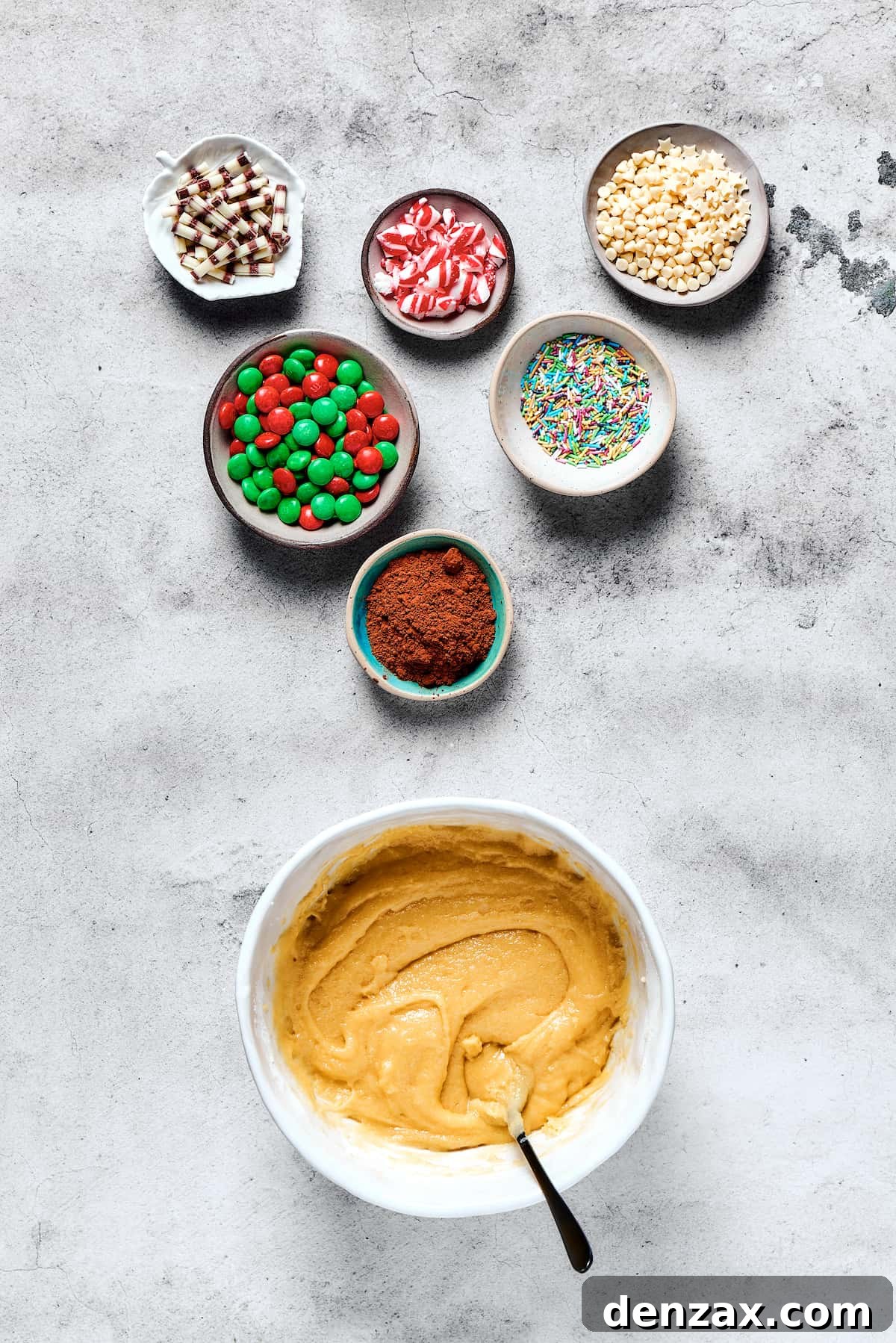 A bowl of creamy, unflavored cookie dough is displayed alongside small dishes filled with vibrant M&M's and sprinkles, ready for festive decoration.