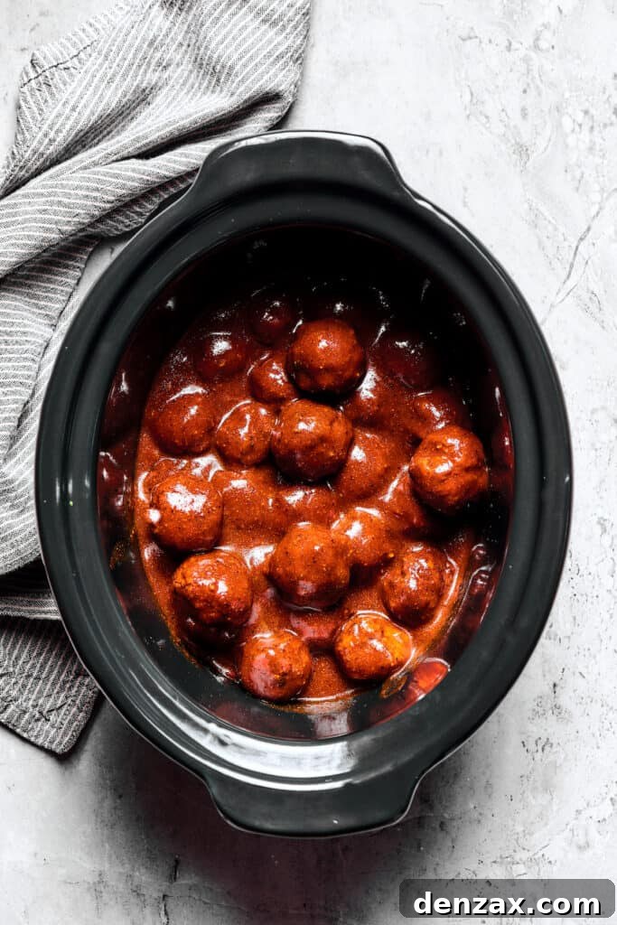 A slow cooker viewed from the top, filled with grape jelly meatballs.
