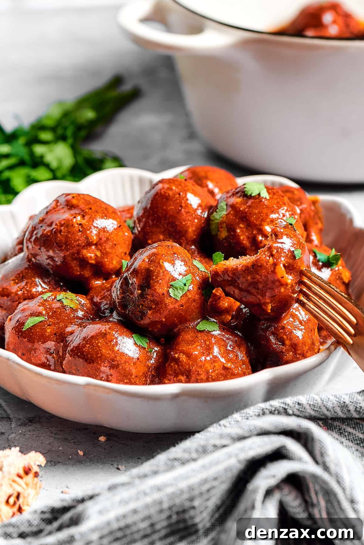A large white dish of grape jelly meatballs, with a smaller plate of them nearby.