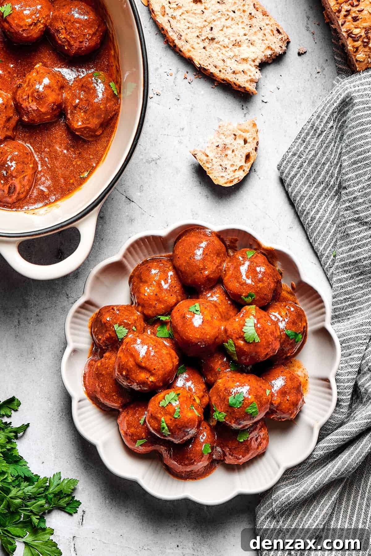 A plate with fluted edges, heaped with grape jelly meatballs, next to a larger serving dish.
