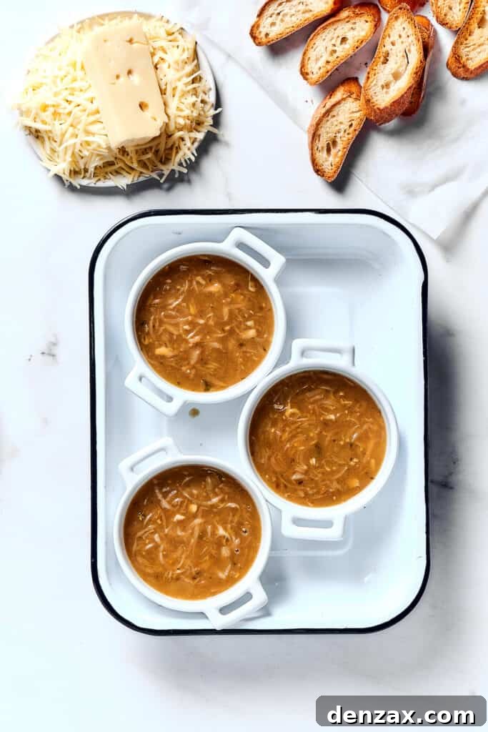 Individual oven-proof bowls of French onion soup, with baguette slices and shredded cheese nearby.