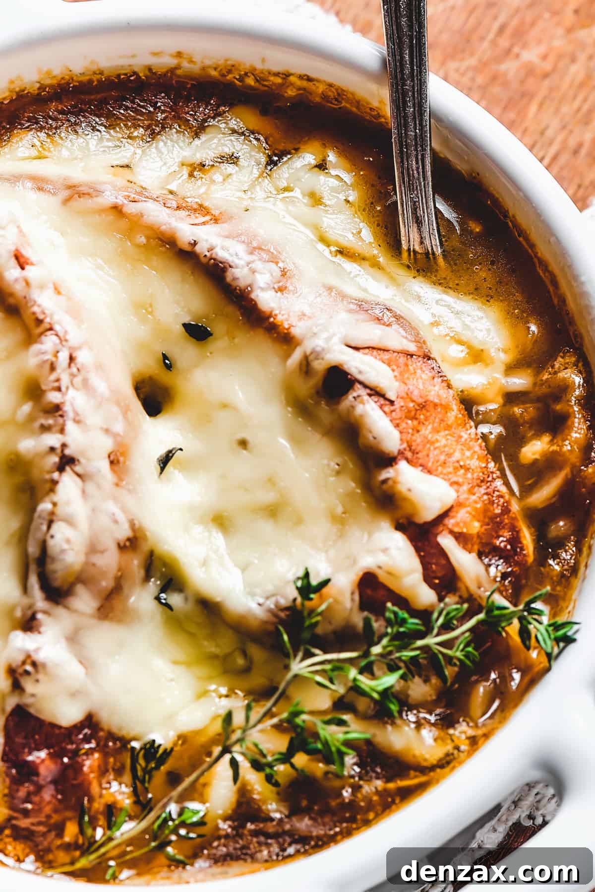 Close-up shot of French Onion Soup, showcasing the melted cheese and a fresh thyme garnish.