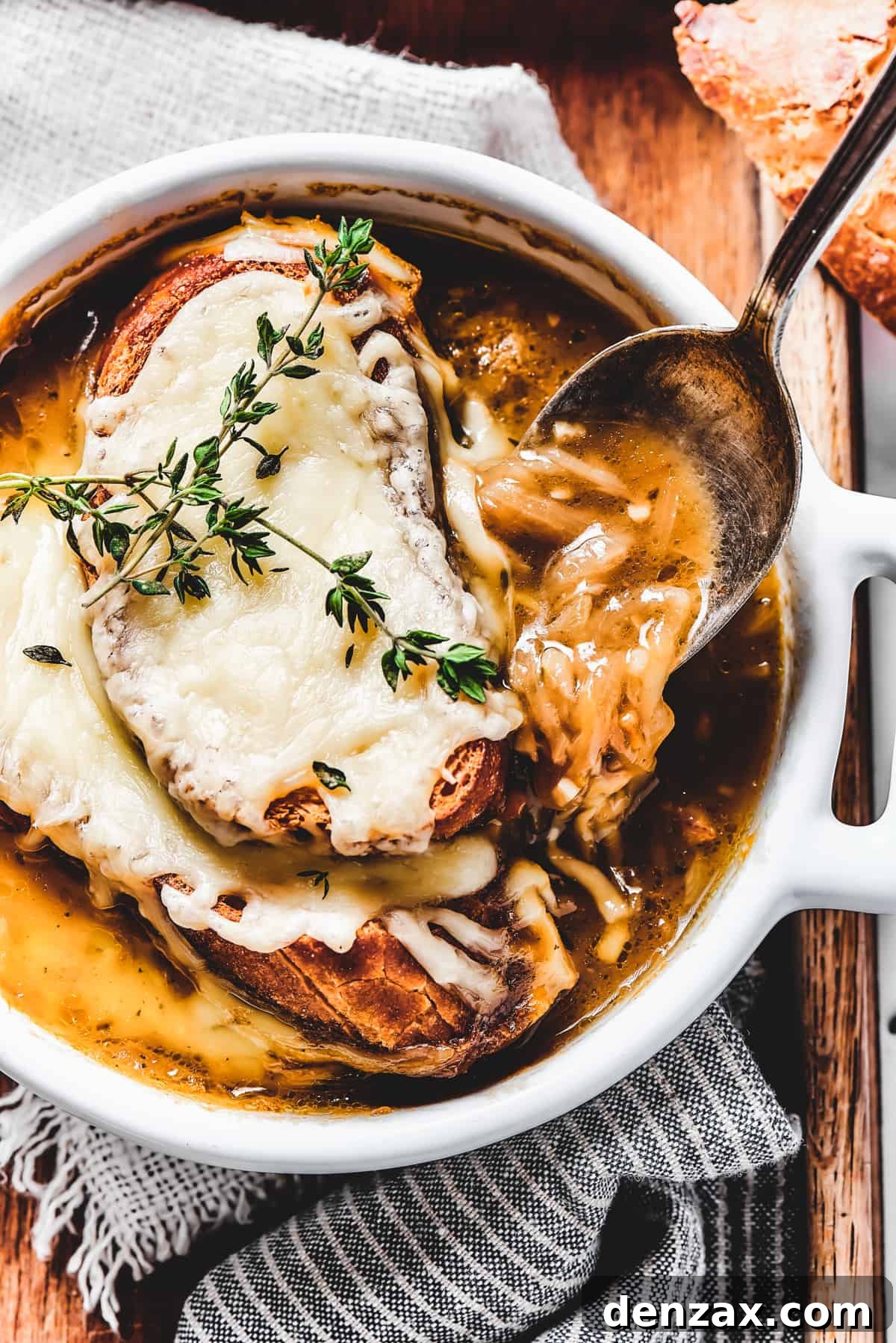 A spoon scooping French Onion Soup from a bowl, showing the melted cheese.