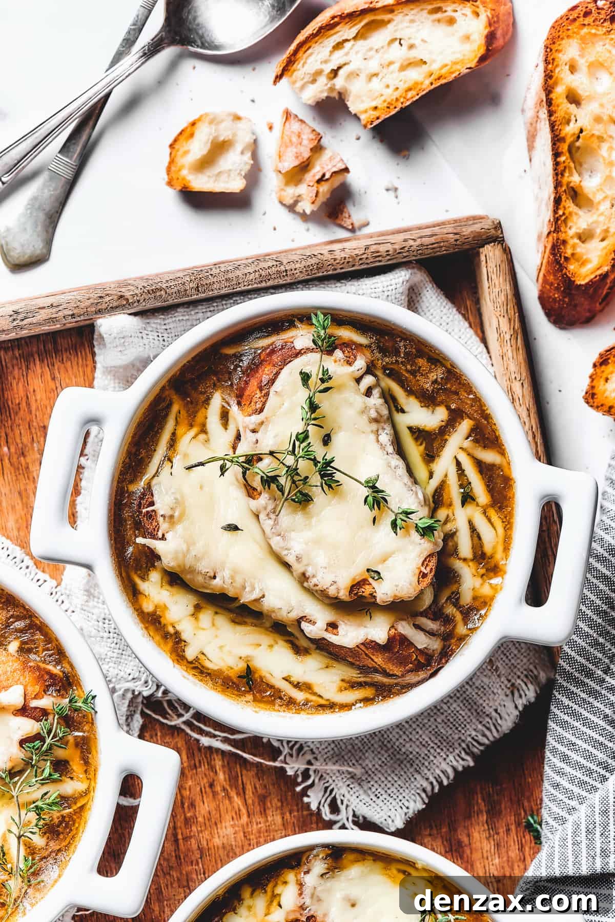 Double-handled bowls of French onion soup on a rustic wooden tray.