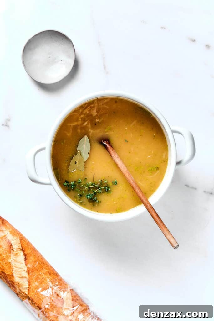 French Onion Soup simmering in a pot with fresh bay leaves and thyme sprigs.