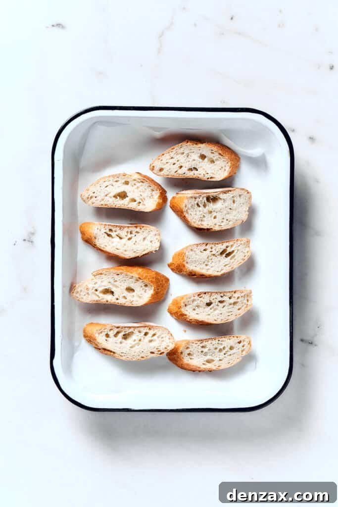 Slices of French baguette arranged on a baking sheet, ready for toasting.