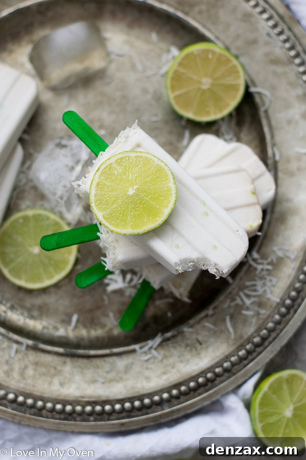 A hand holding a beautifully creamy coconut lime popsicle with a textured coconut topping.