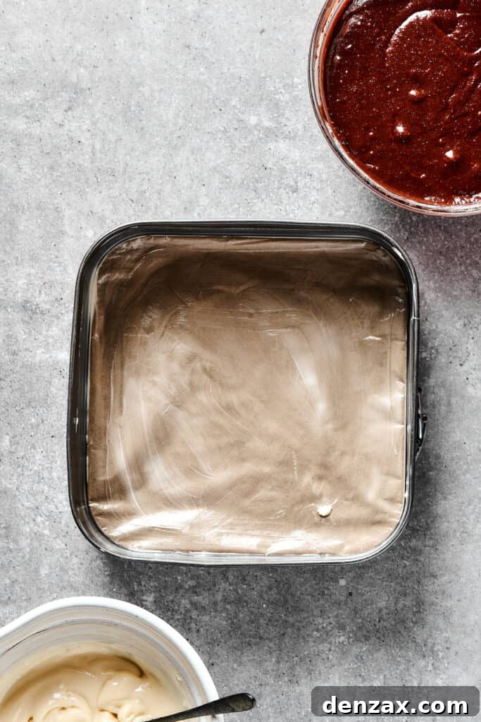 Marbled Chocolate Cheesecake Brownies 6 A 9x9 inch baking dish meticulously lined with parchment paper, ready for brownie batter.