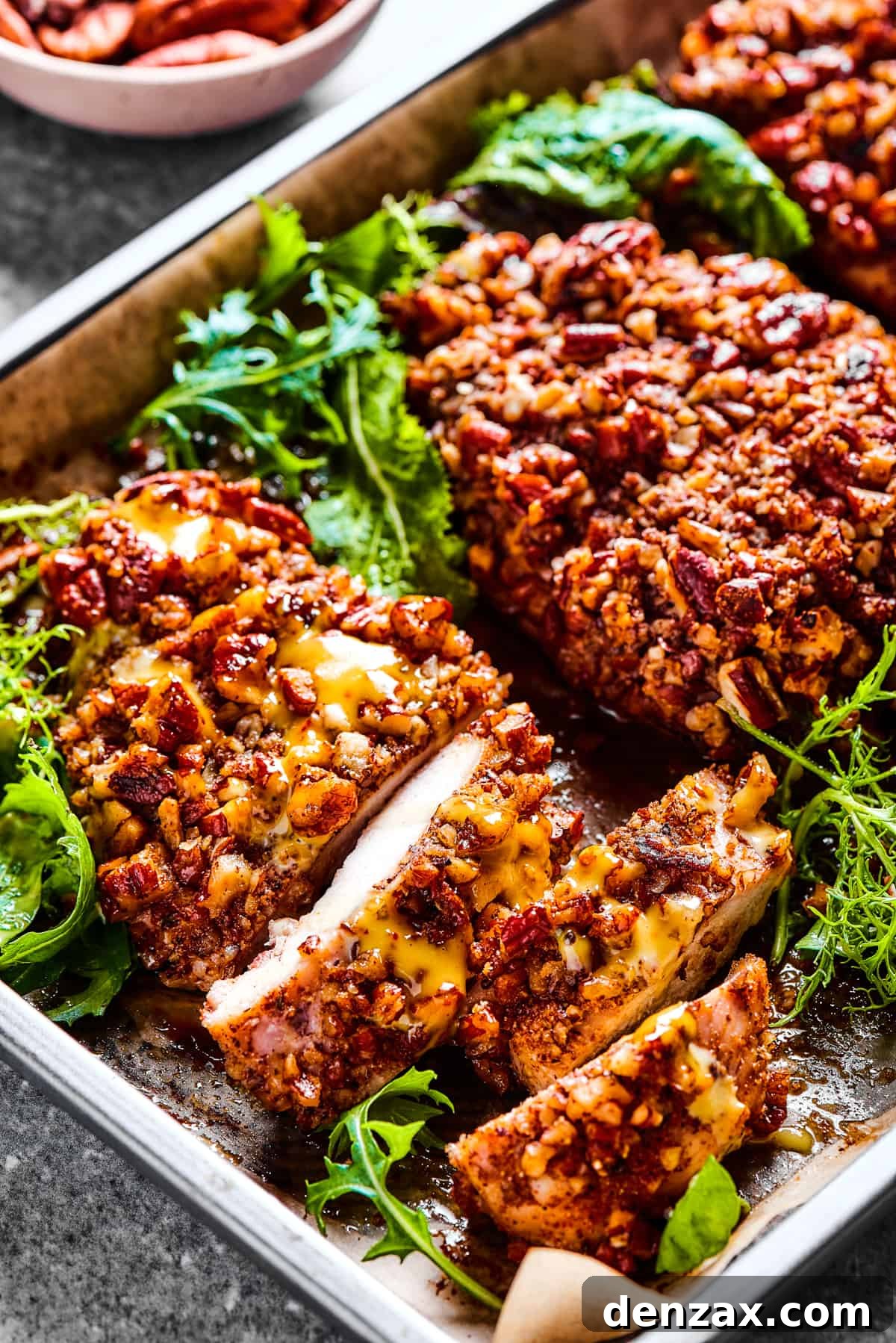 Golden-brown pecan crusted chicken breasts artfully arranged in a sleek stainless steel serving dish, ready to be presented.