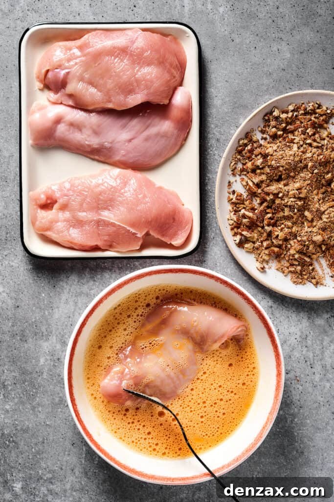 The initial step of breading: raw chicken being immersed in a bowl of beaten eggs, preparing it for the pecan coating.