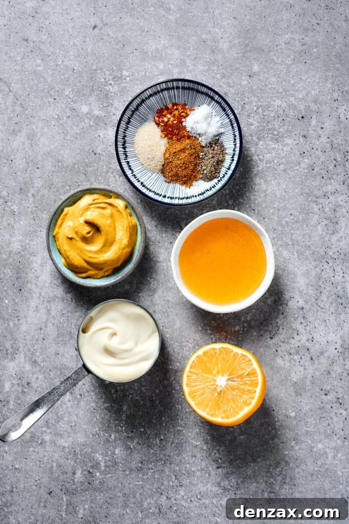 An array of ingredients for honey mustard sauce: a small dish of spices, a jar of golden honey, a vibrant sliced lemon, a dollop of creamy mayonnaise, and a squeeze of mustard.