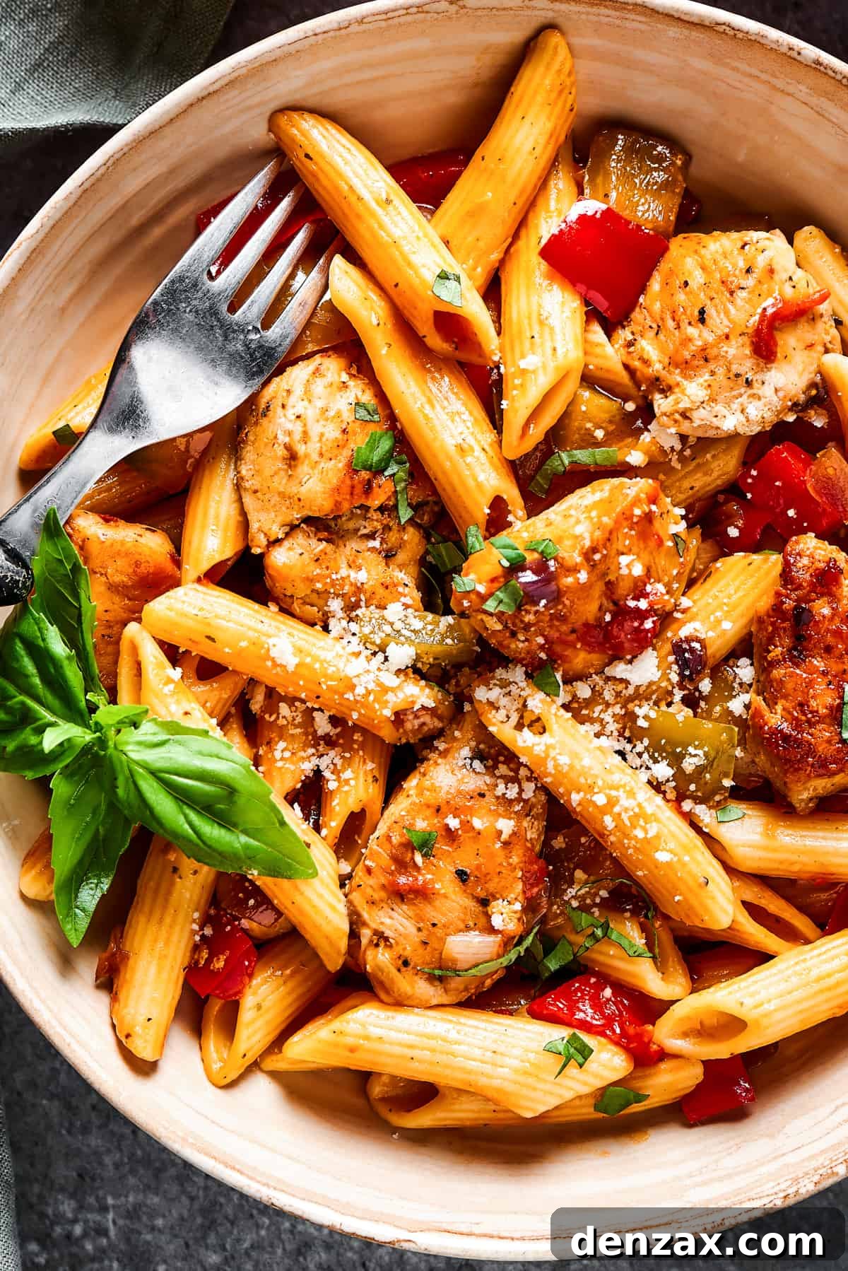 Light yet hearty Chicken Fajita Pasta is made with juicy chicken and crisp-tender veggies. An easy, perfect family dinner recipe! overhead close up of chicken and penne with tomatoes, peppers, and onions.