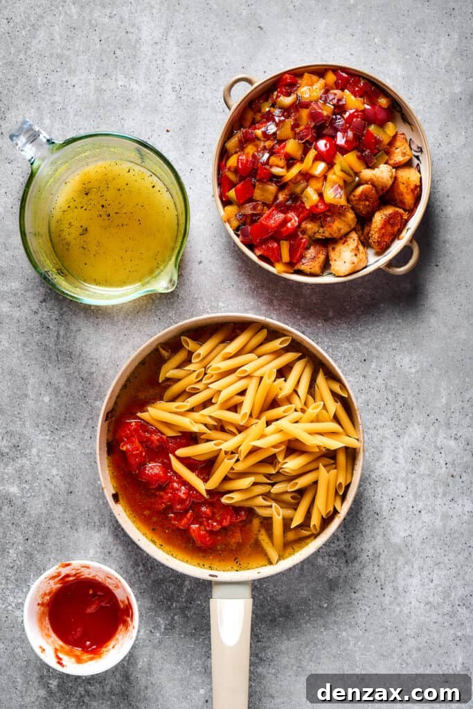 This Chicken Fajita Pasta, prepared with tender veggies and juicy chicken, makes the perfect dinner for family night or a casual get-together with friends. Pasta, tomatoes, and broth combined in a skillet next to a dish of cooked chicken and vegetables.