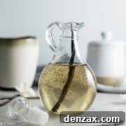 A bottle of homemade vanilla bean syrup next to fresh vanilla beans.