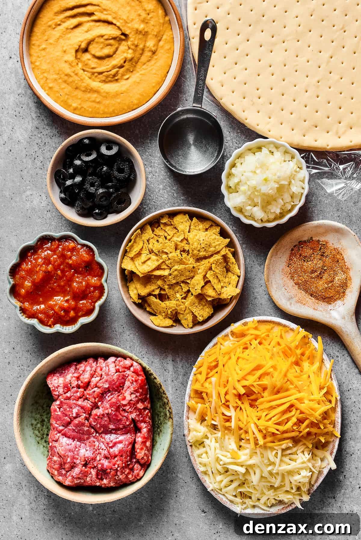From top: refried beans, pizza crust, black olives, water, onion, salsa, crushed tortilla chips, taco seasoning, ground beef, cheese.
