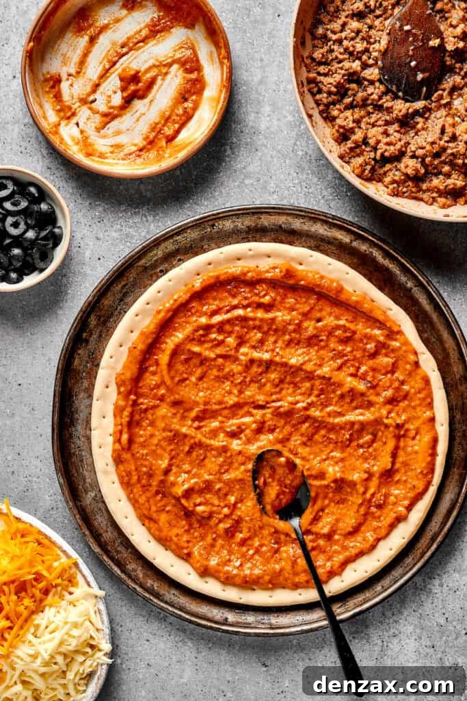 Spreading refried bean sauce on a prepared pizza crust.
