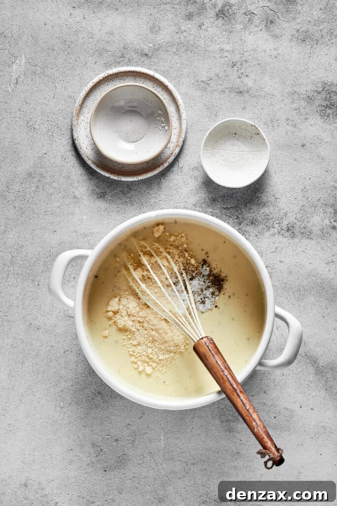 A creamy sauce being whisked to a smooth consistency in a large skillet.