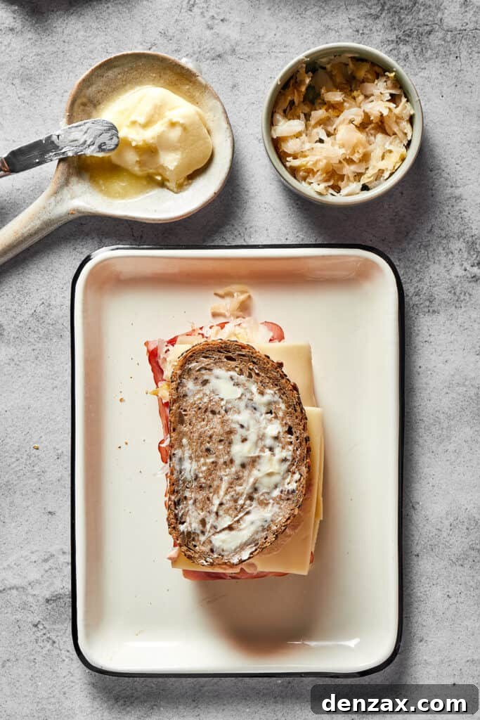 A fully assembled, un-grilled Reuben sandwich, with all its layers neatly stacked between two slices of rye bread, awaiting the grill.