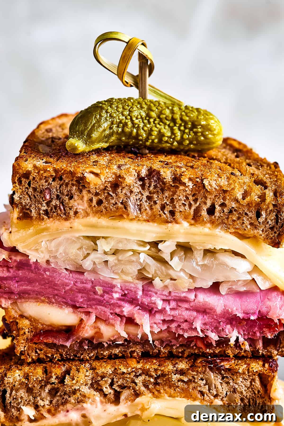 A magnificent Reuben sandwich, cut into two perfect halves and elegantly stacked, is held together with a decorative skewer, showcasing its rich layers of ingredients.