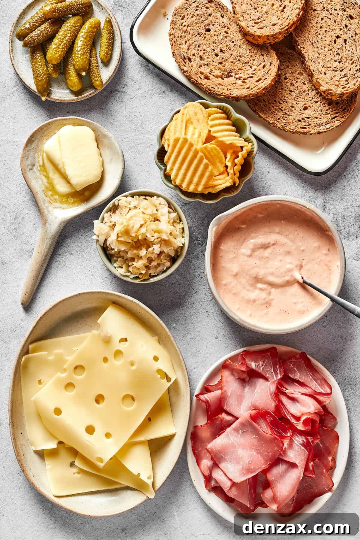 A vibrant display of fresh ingredients for a Reuben sandwich, including dill pickles, slices of rye bread, crispy potato chips, a bowl of creamy Russian dressing, thinly sliced corned beef, delicate Swiss cheese, and tangy sauerkraut, arranged artfully with a pat of butter.