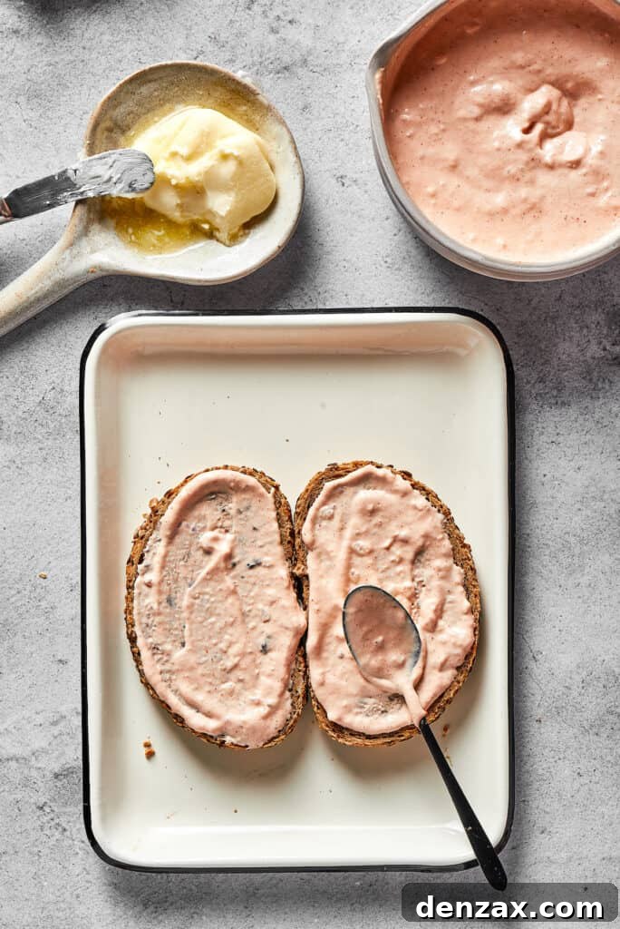 A generous, thick layer of creamy Russian dressing is spread onto the unbuttered side of a slice of rye bread, ready for the sandwich assembly.