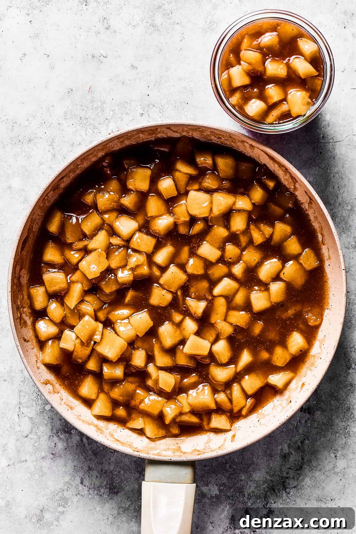 A skillet filled with rich, golden homemade apple pie filling, with a small glass jar of the same filling beside it, ready for storage or immediate use.
