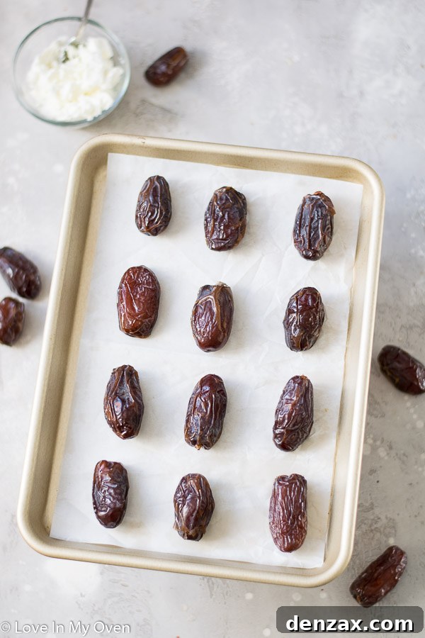 Dates on a parchment-lined baking sheet, showing a slit cut lengthwise to remove the pit.
