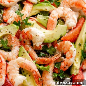 cooked shrimp, avocado slices, and salad greens tossed together in a white serving bowl