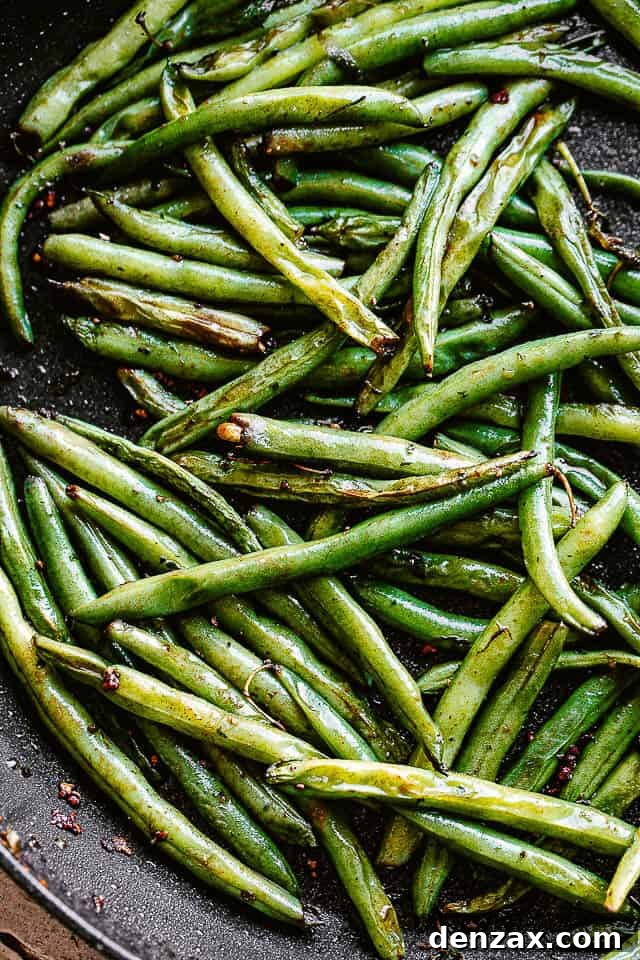 Close-up of fresh green beans being pan-fried in a skillet with oil