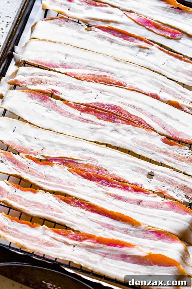 Raw bacon slices laid out in a single layer on a wire rack over a parchment-lined baking sheet, ready for the oven.